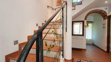Una escalera con barandilla de cristal, piso de baldosas y alfombra estampada.