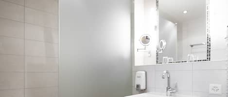Une salle de bain moderne avec une douche à l’italienne en verre, un lavabo blanc avec un meuble-vasque en bois et un grand miroir.