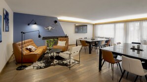 A modern living room with a sofa, armchairs, a coffee table, a dining table with chairs, a fireplace, and a large window with curtains. - Olympic (Crans-Montana)