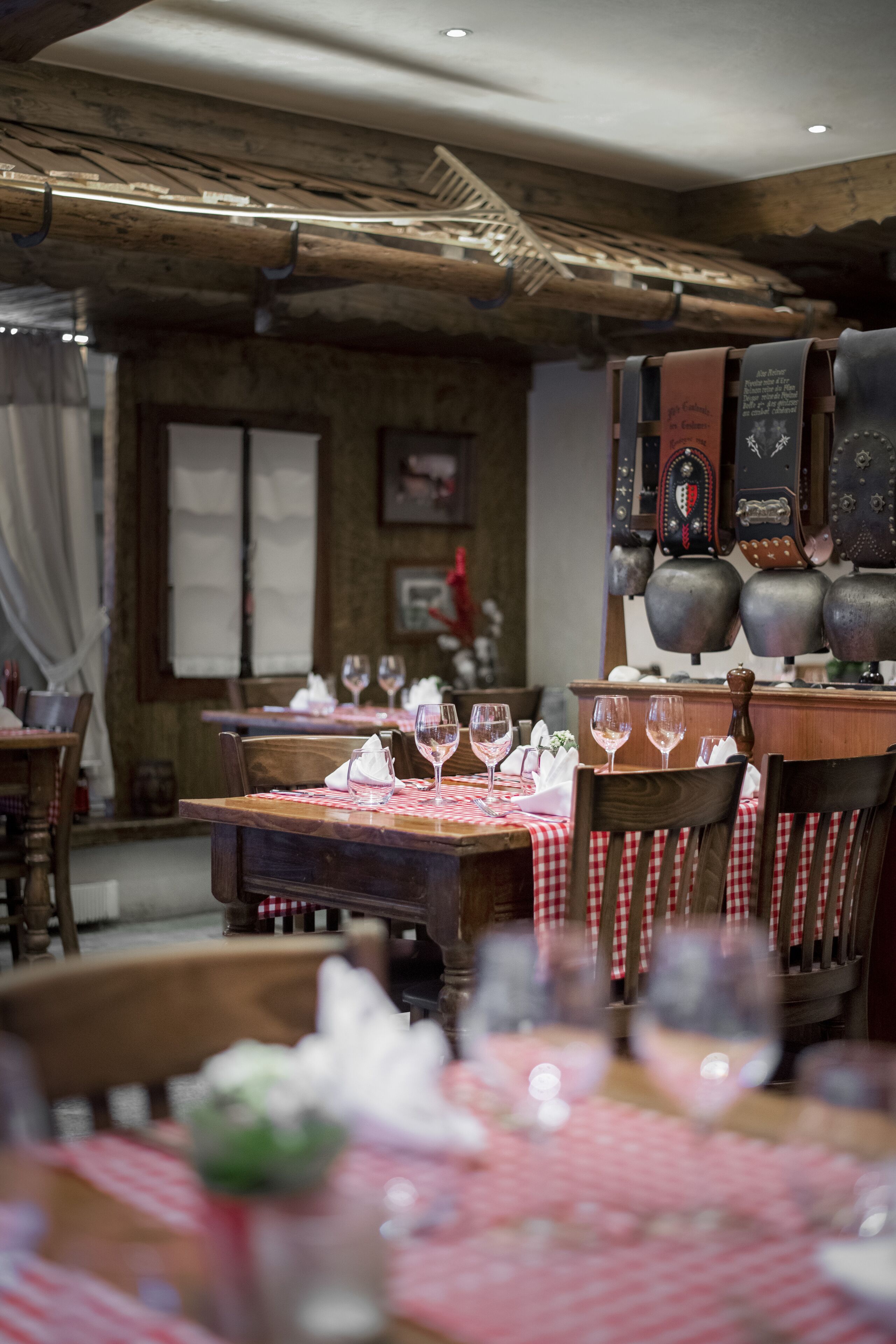 Restaurante com mesas e cadeiras de madeira, toalhas xadrez vermelhas e brancas, e copos de vinho dispostos para uma refeição.