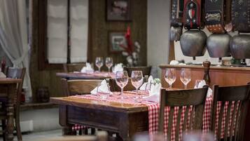Restaurante com mesas e cadeiras de madeira, toalhas xadrez vermelhas e brancas, e copos de vinho dispostos para uma refeição.