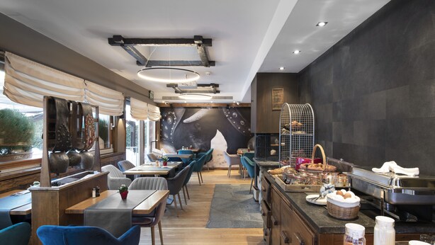 A restaurant with wooden tables and chairs, a buffet area with food and drinks, and a large mural on the wall. - Olympic (Crans-Montana)