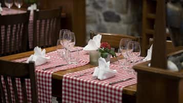 Una mesa de comedor con mantel a cuadros rojos y blancos, copas de vino y un jarrón con flores rojas.