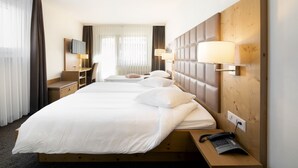 A hotel room with two beds, a desk, a chair, a TV, and a lamp. - Olympic (Crans-Montana)