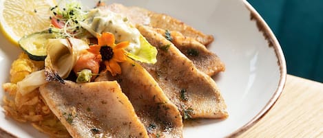A plate with fish fillets, lemon, and vegetables.