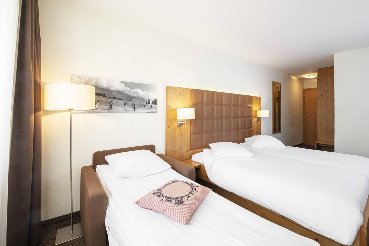 Quarto de hotel com duas camas, cabeceira, abajures, um quadro na parede e uma porta de madeira.