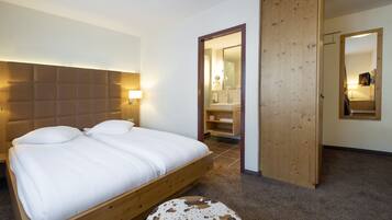 Un dormitorio con una cama de madera, un reposapiés redondo y un baño visible a través de una puerta abierta.