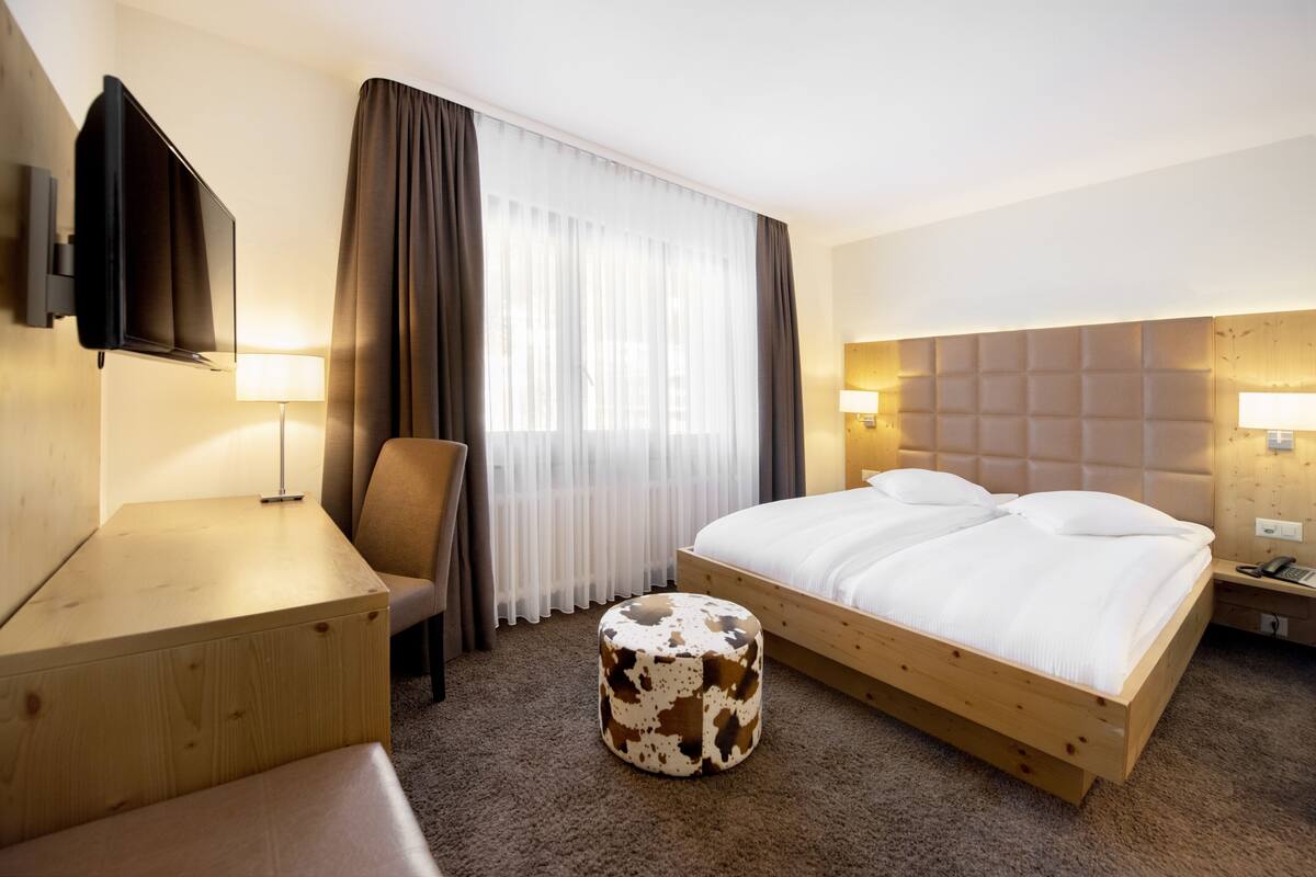 Quarto de hotel com cama, escrivaninha, cadeira, televisão e luminária.
