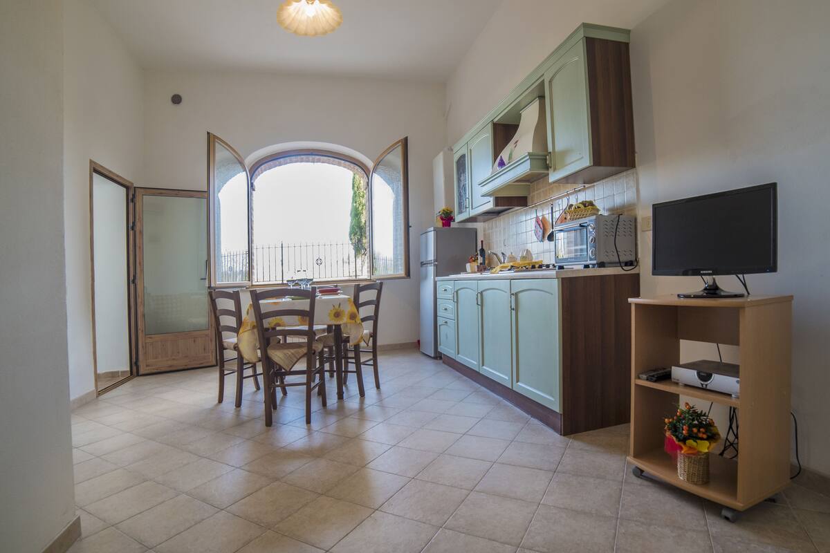 A kitchen with a dining table, chairs, a microwave, a TV, and cabinets.