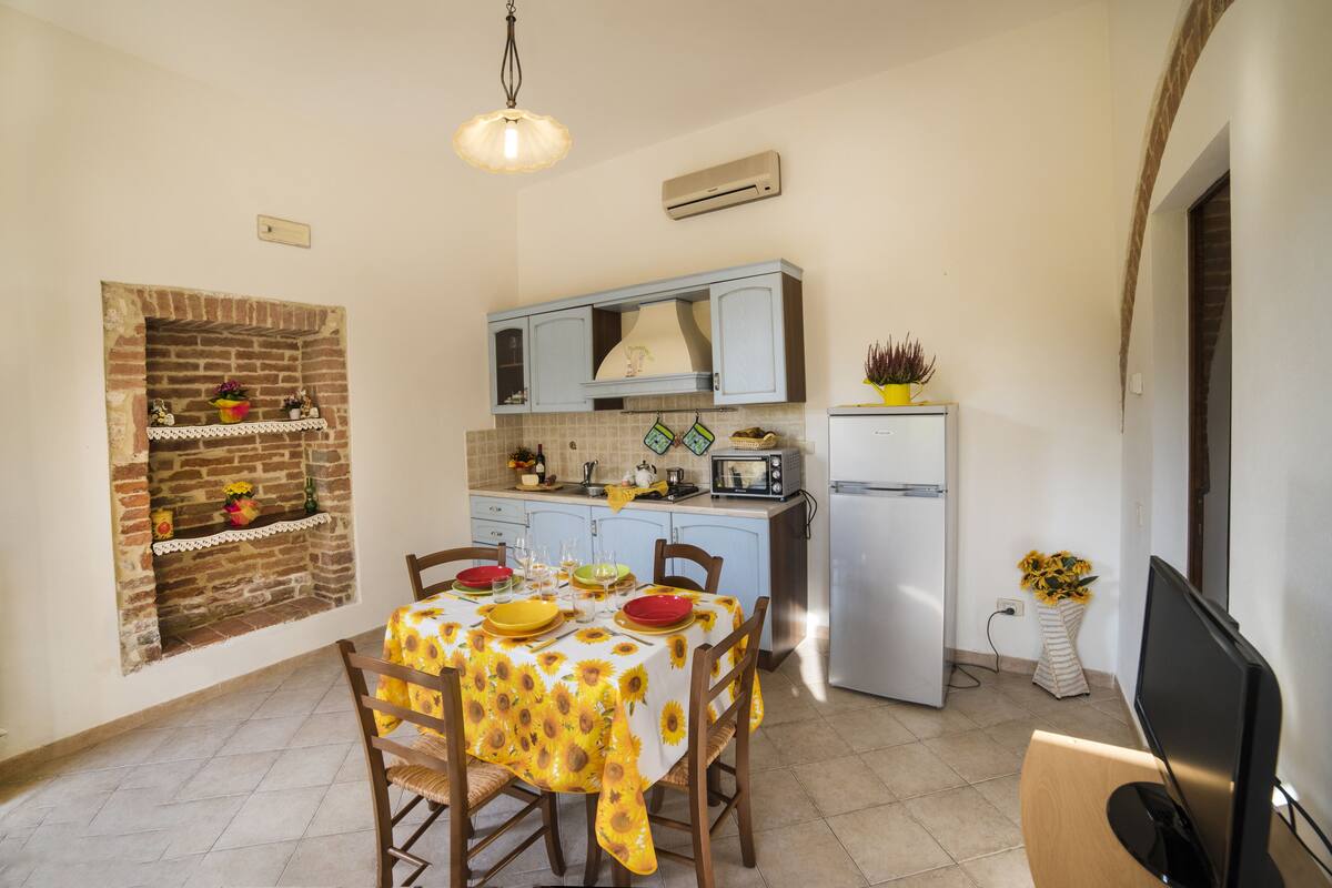 A compact kitchen with a brick fireplace, a dining table set with yellow tablecloth, and a TV on a wooden stand.