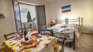 A dining area with a table set for two, featuring a wooden board with food and a bottle of wine. A bed with a floral bedspread is visible in the background. - Casa Santa Caterina (Asciano)