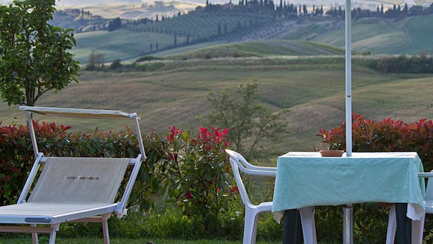A poolside area with a view of rolling hills, a table with a tablecloth, and two lounge chairs. - Casa Santa Caterina (Asciano)