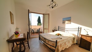 A bedroom with a bed, a desk, a chair, a small table, and a cabinet. There is a window with a view of the outside. - Casa Santa Caterina (Asciano)