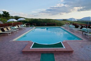 A rectangular swimming pool with a brick border, surrounded by lounge chairs and umbrellas. - Casa Santa Caterina (Asciano)