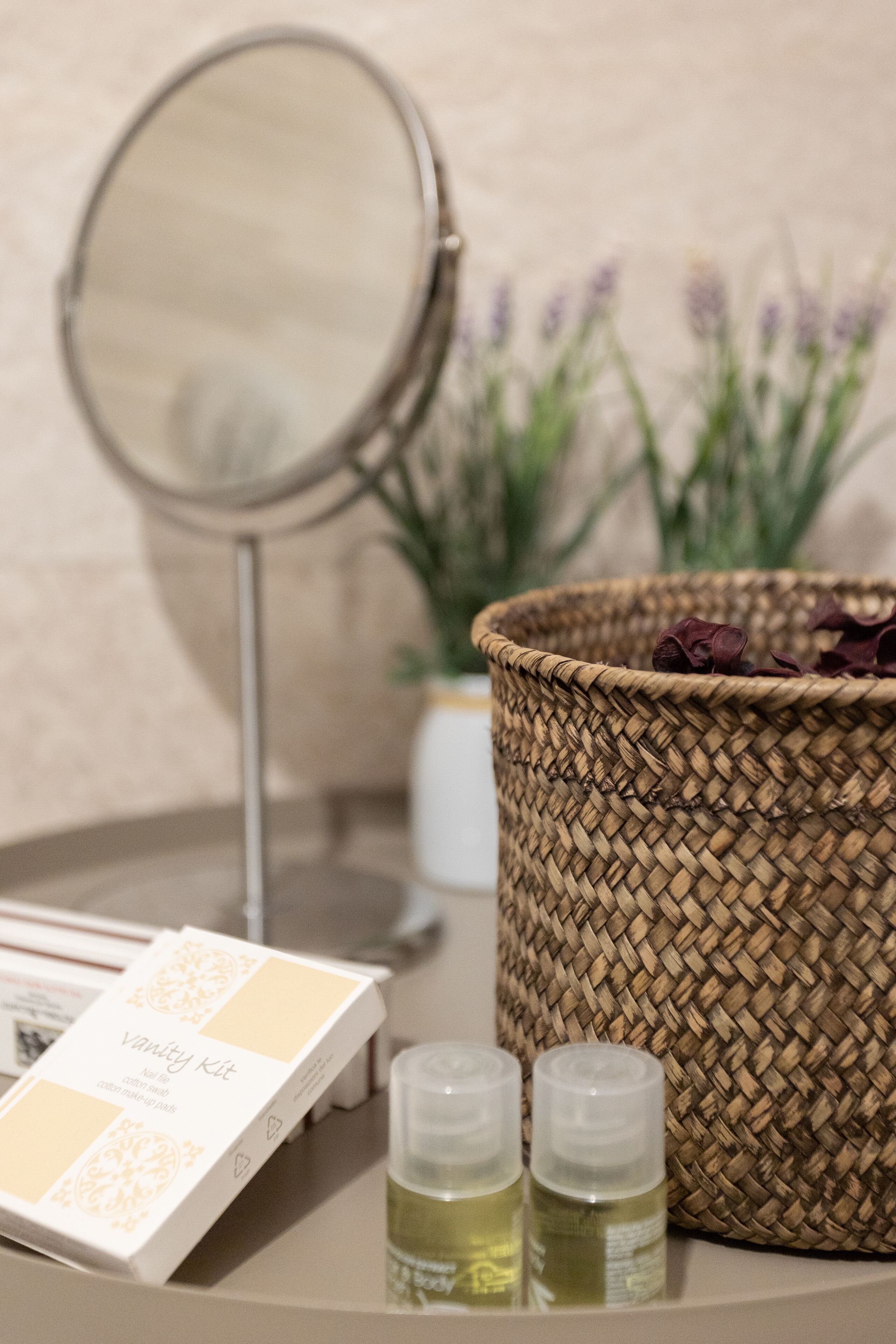 Um kit de higiene com espelho, duas embalagens de loção e uma cesta de palha com lavanda seca.