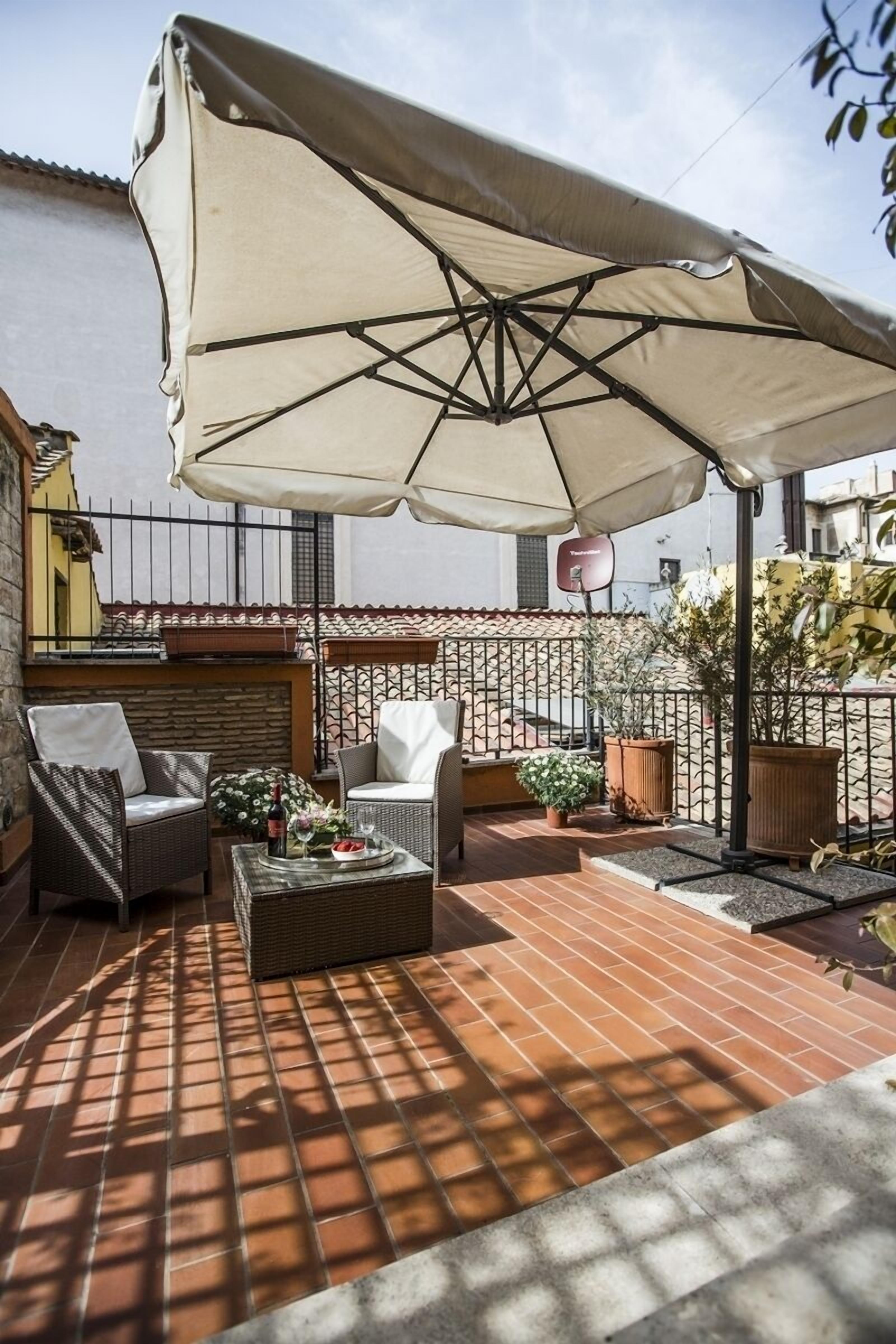 An outdoor patio with wicker furniture, a table with drinks, and a large umbrella providing shade.