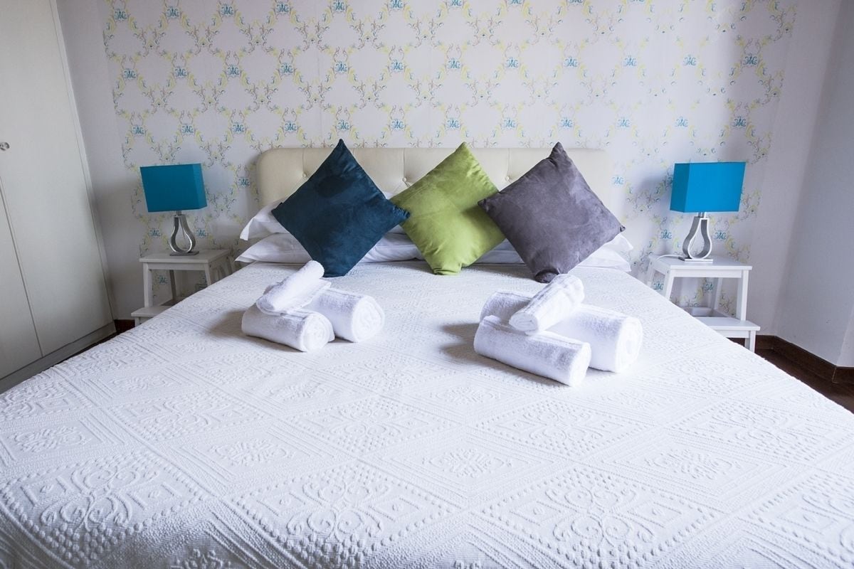 Un lit bien fait, avec du linge de lit blanc, quatre oreillers de couleurs différentes et deux lampes de chevet posées sur des tables de chevet blanches.