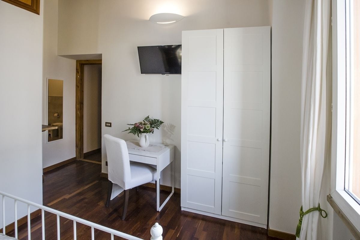 A room with a white desk, a chair, a TV mounted on the wall, and a wardrobe.