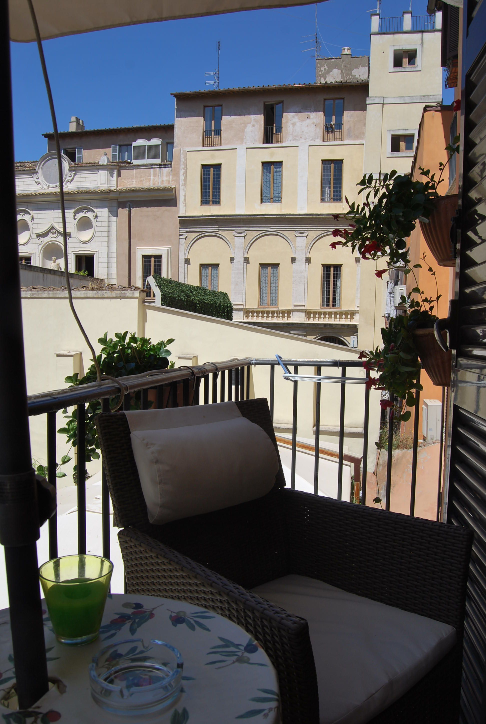 Un balcone con mobili in vimini, un tavolino in vetro e una pianta in vaso.