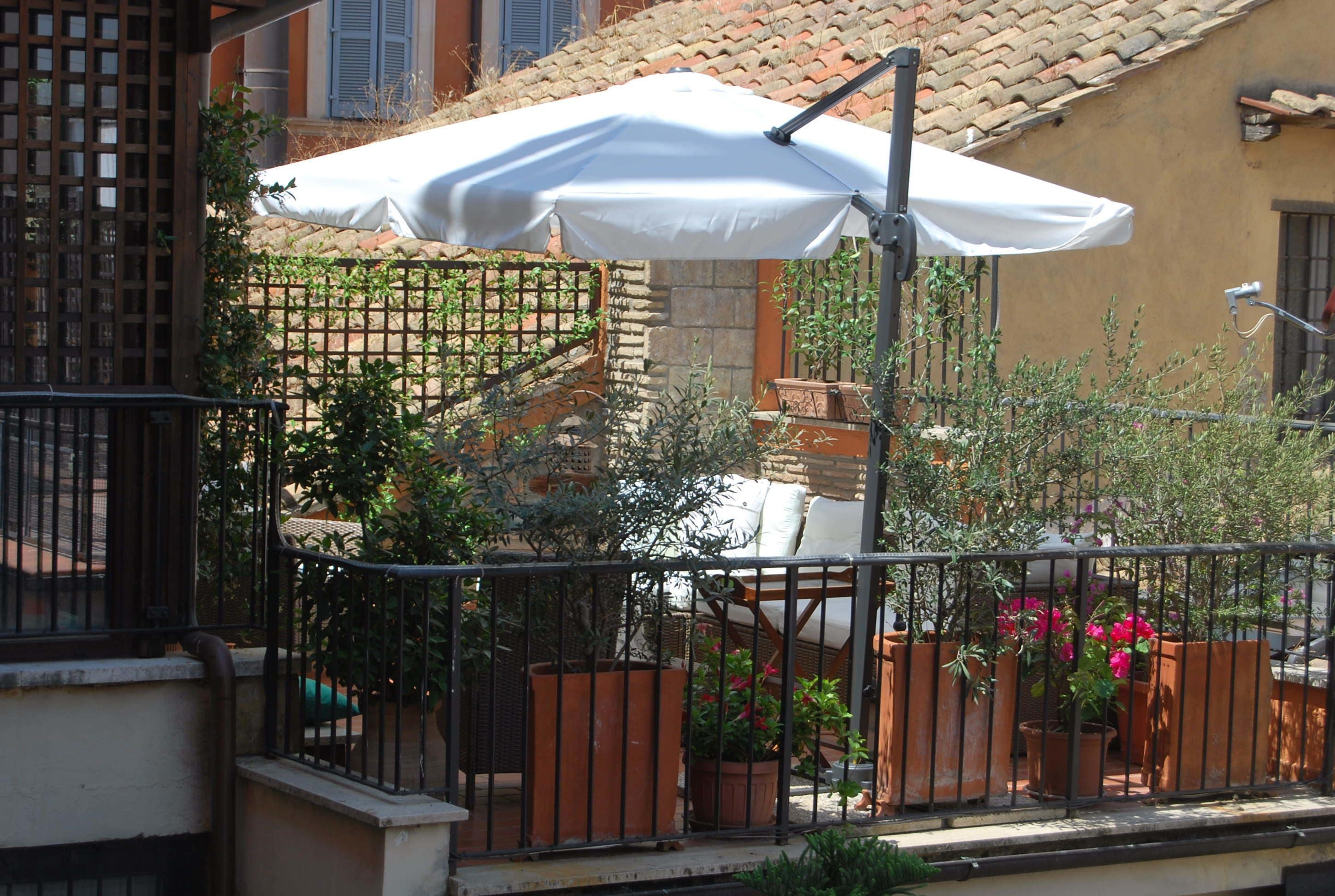 Un balcon agrémenté d’un parasol blanc, de plantes en pot et d’une rambarde en métal.