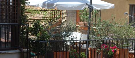 Un balcon agrémenté d’un parasol blanc, de plantes en pot et d’une rambarde en métal.