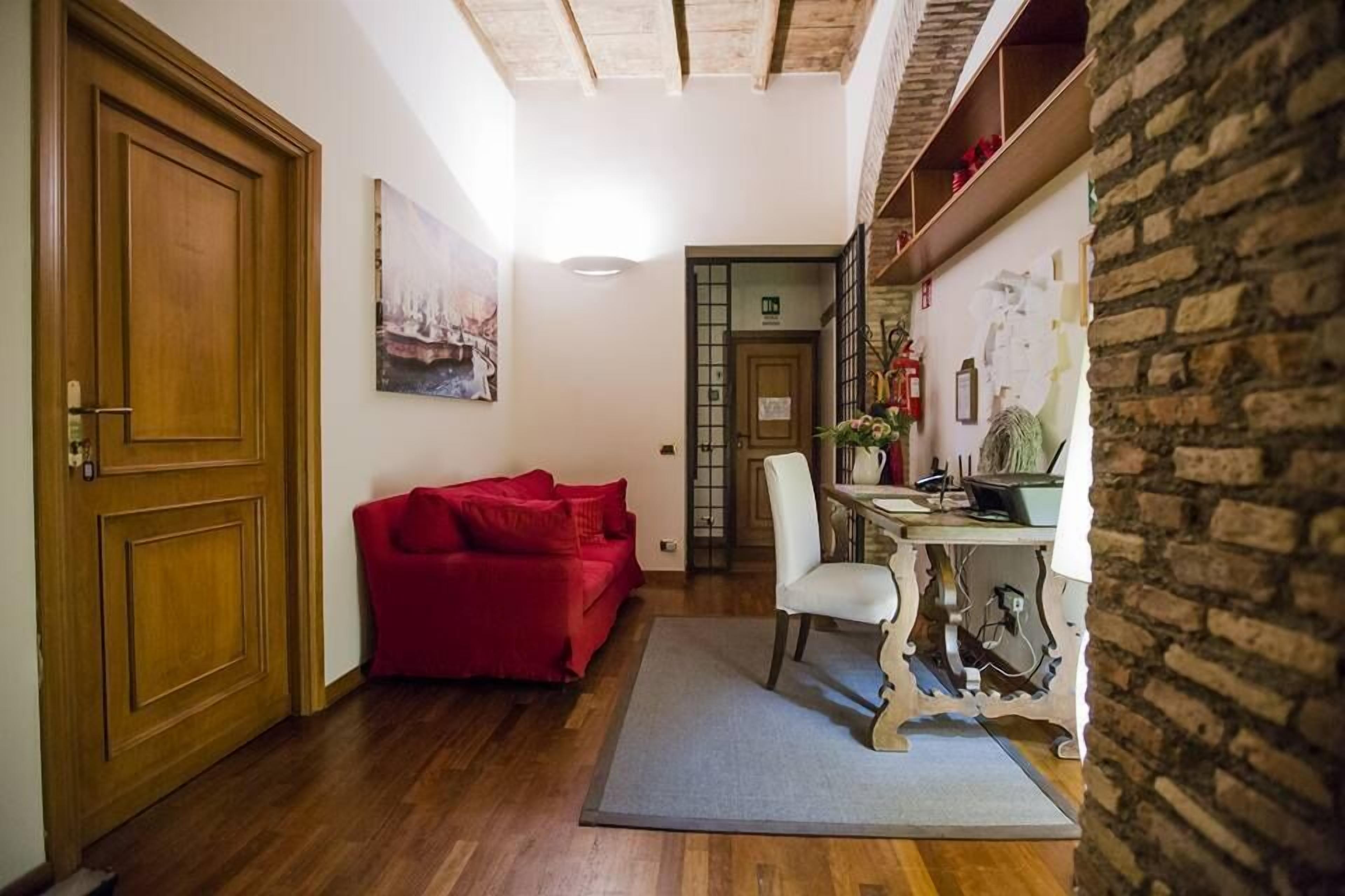 A cozy room with a wooden door, a red sofa, a white chair, and a table with a laptop.