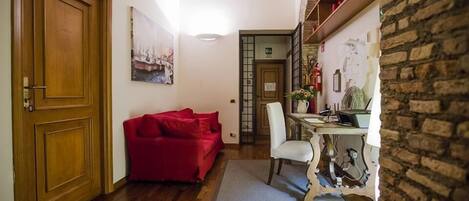 A cozy room with a wooden door, a red sofa, a white chair, and a table with a laptop.