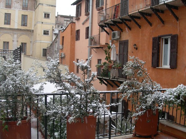 Un balcon orné de plantes en pot, un escalier et la façade d’un immeuble agrémentée de balcons et de fenêtres.