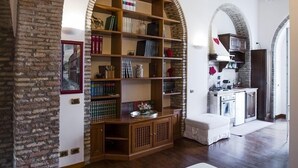 A cozy room with a wooden bench, a bookshelf, and a kitchen area visible through an archway. - Pettinary Village (Rome)