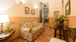 Un accogliente soggiorno con un divano floreale, un tavolo in legno con un vaso di fiori e una lampada.