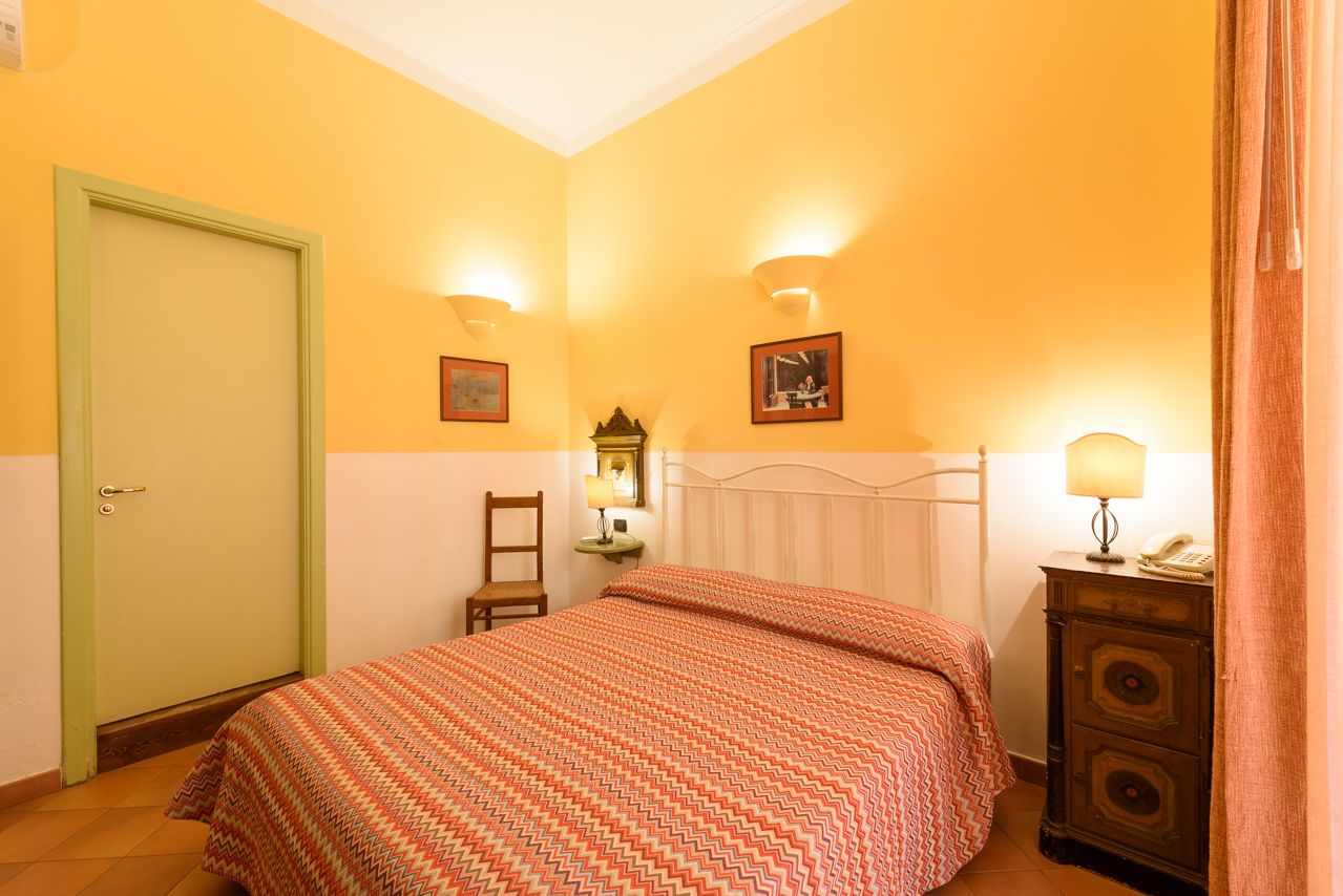 A bedroom with a bed, a nightstand, a lamp, and a door.