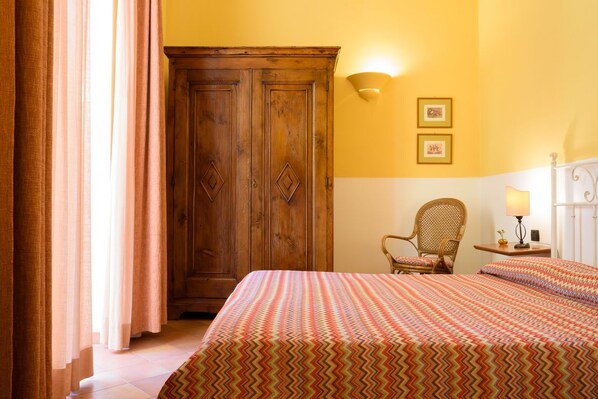 A bedroom with a bed, a wooden wardrobe, a chair, and a nightstand with a lamp. - Mergellina (Naples)