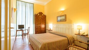 Una camera d'albergo con un letto, una scrivania con un computer, un armadio e una sedia.