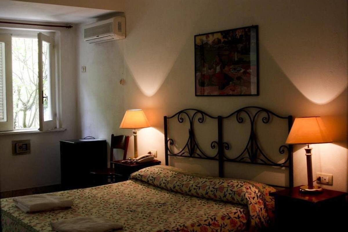 Une chambre à coucher comprenant un lit, deux lampes de chevet, une table de chevet, une chaise, un bureau et une fenêtre avec des rideaux.