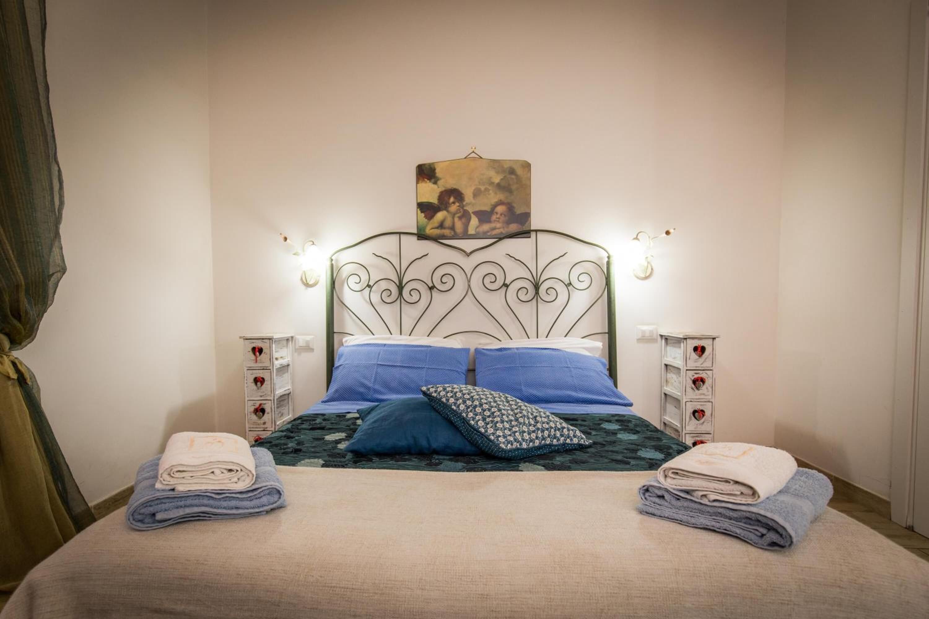 A neatly made bed with blue and white bedding, two bedside tables with heart-shaped drawers, and a wall-mounted picture above the bed.