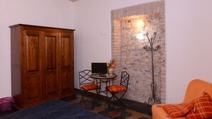 A room with a wooden wardrobe, a small round table with two chairs, a TV, and a brick wall with a light fixture. - All'Ombra del Cupolone (Rome)