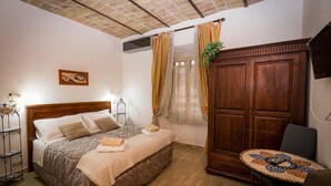 A bedroom with a wooden bed, a small round table, a wardrobe, and a window with curtains. - All'Ombra del Cupolone (Rome)