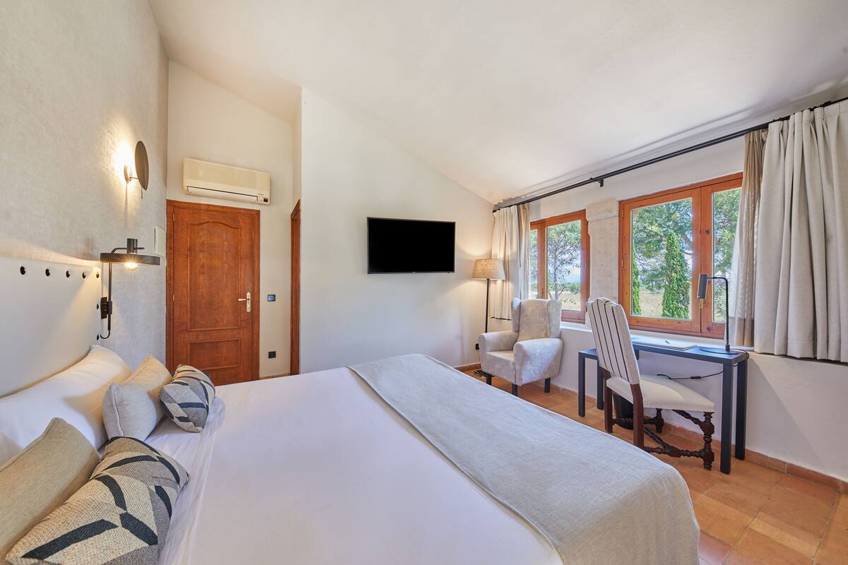 Une chambre d’hôtel avec un lit, un bureau, une chaise, une télévision et une fenêtre avec des rideaux.