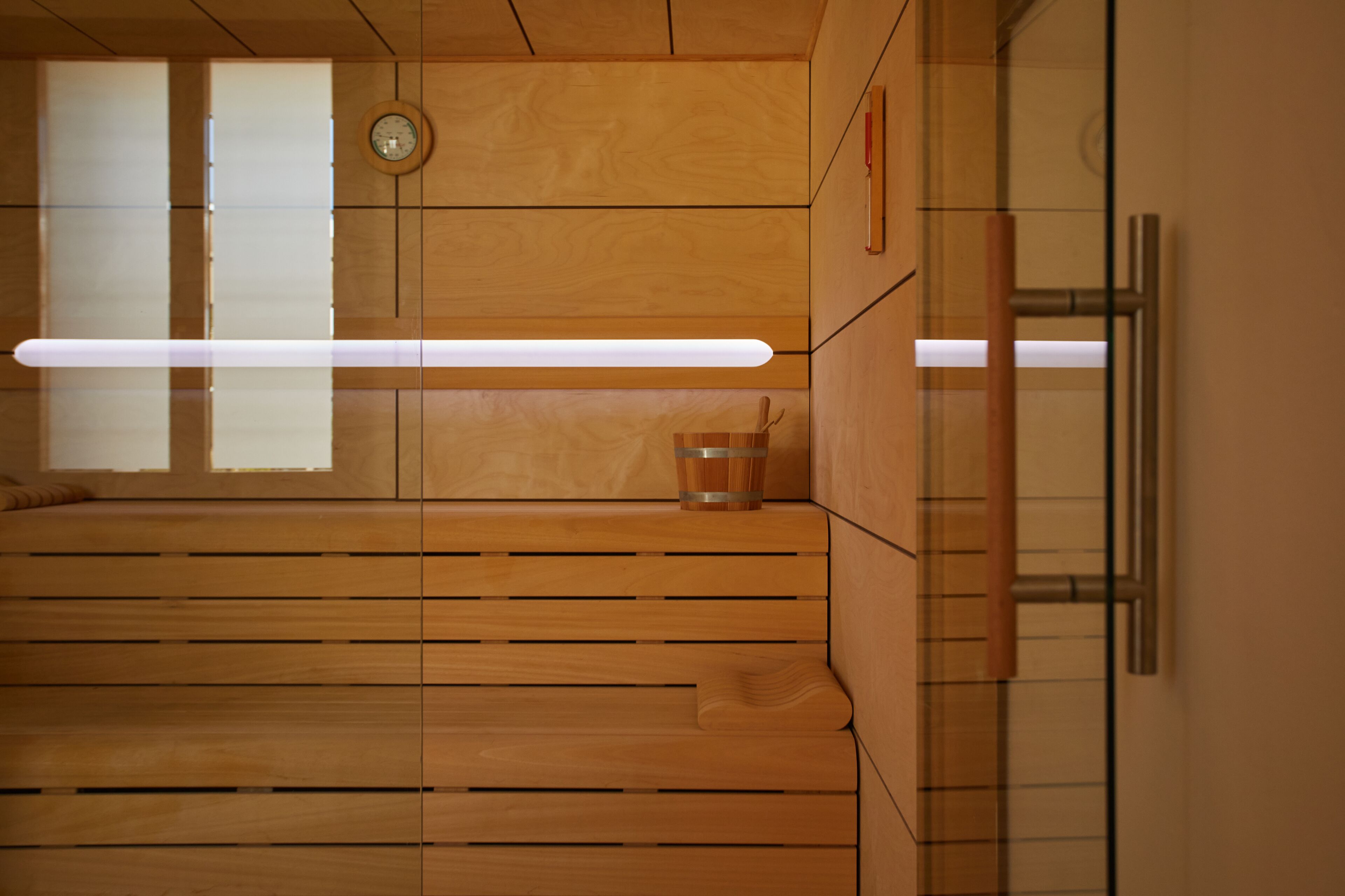 Una habitación moderna con paneles de madera, una lámpara alargada, un reloj y un pequeño taburete de madera.