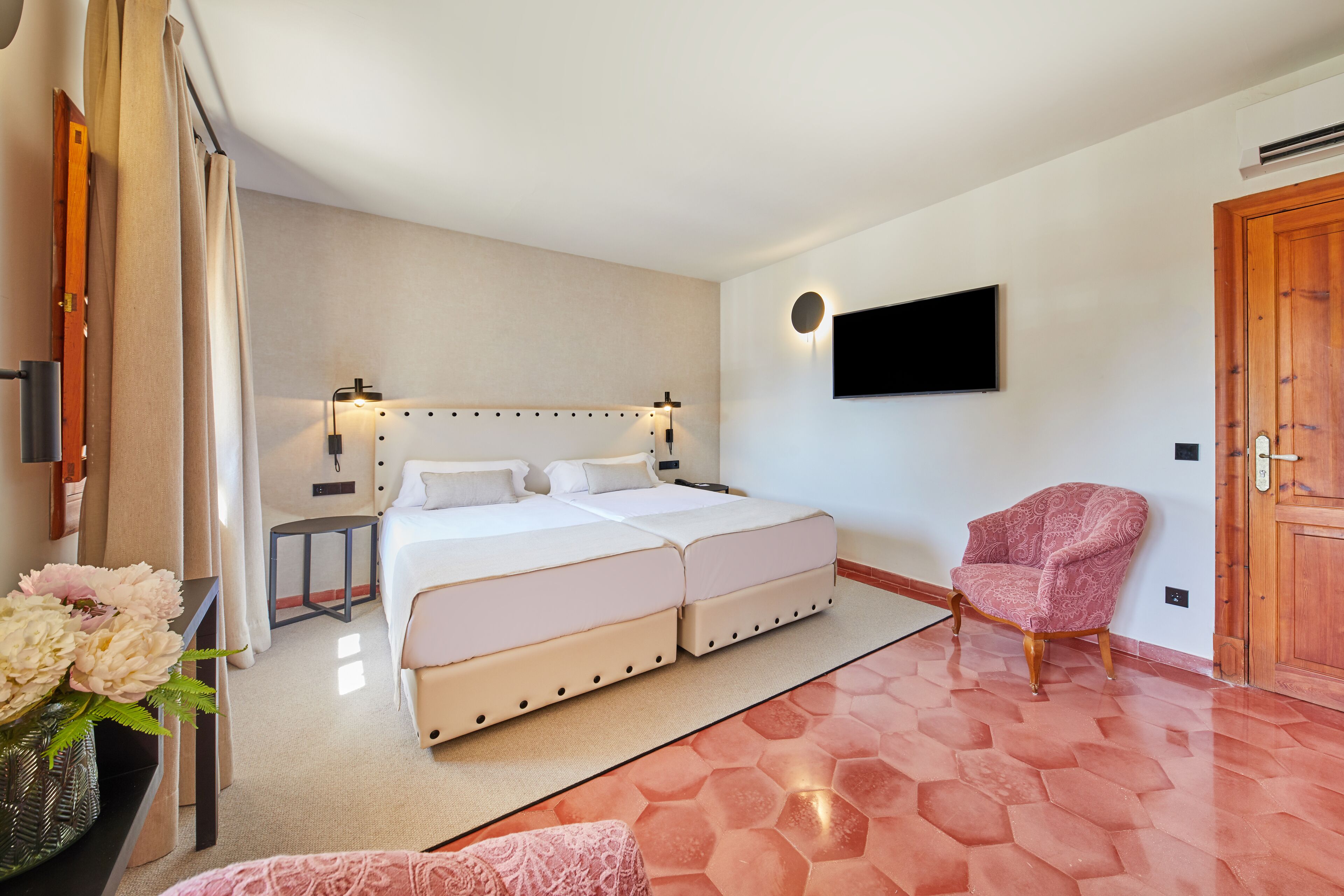Habitación de hotel con cama doble, mesitas de noche, televisor montado en la pared, puerta de madera y una silla estampada.