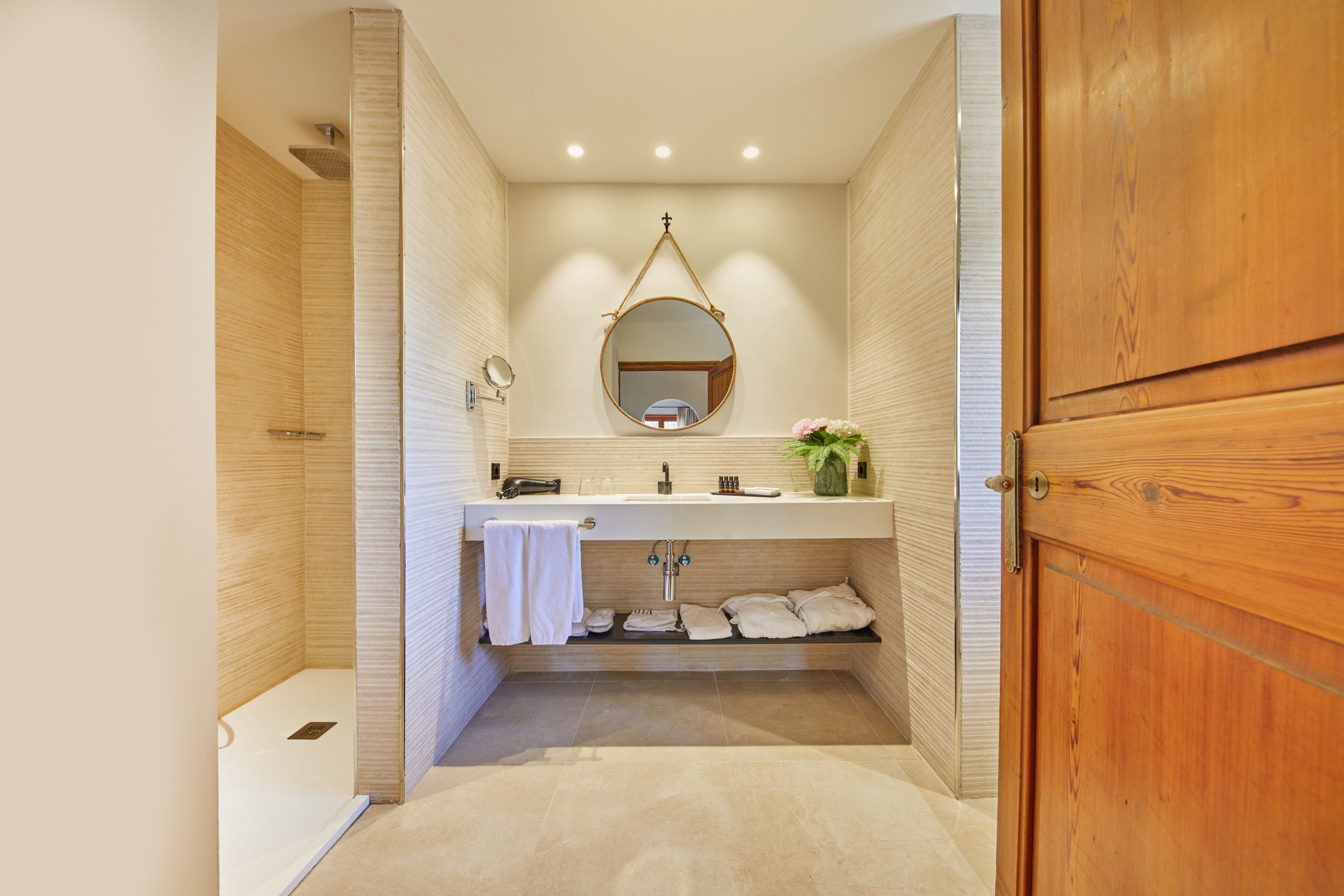 Un baño moderno con tocador de madera, un espejo redondo y zona de ducha.