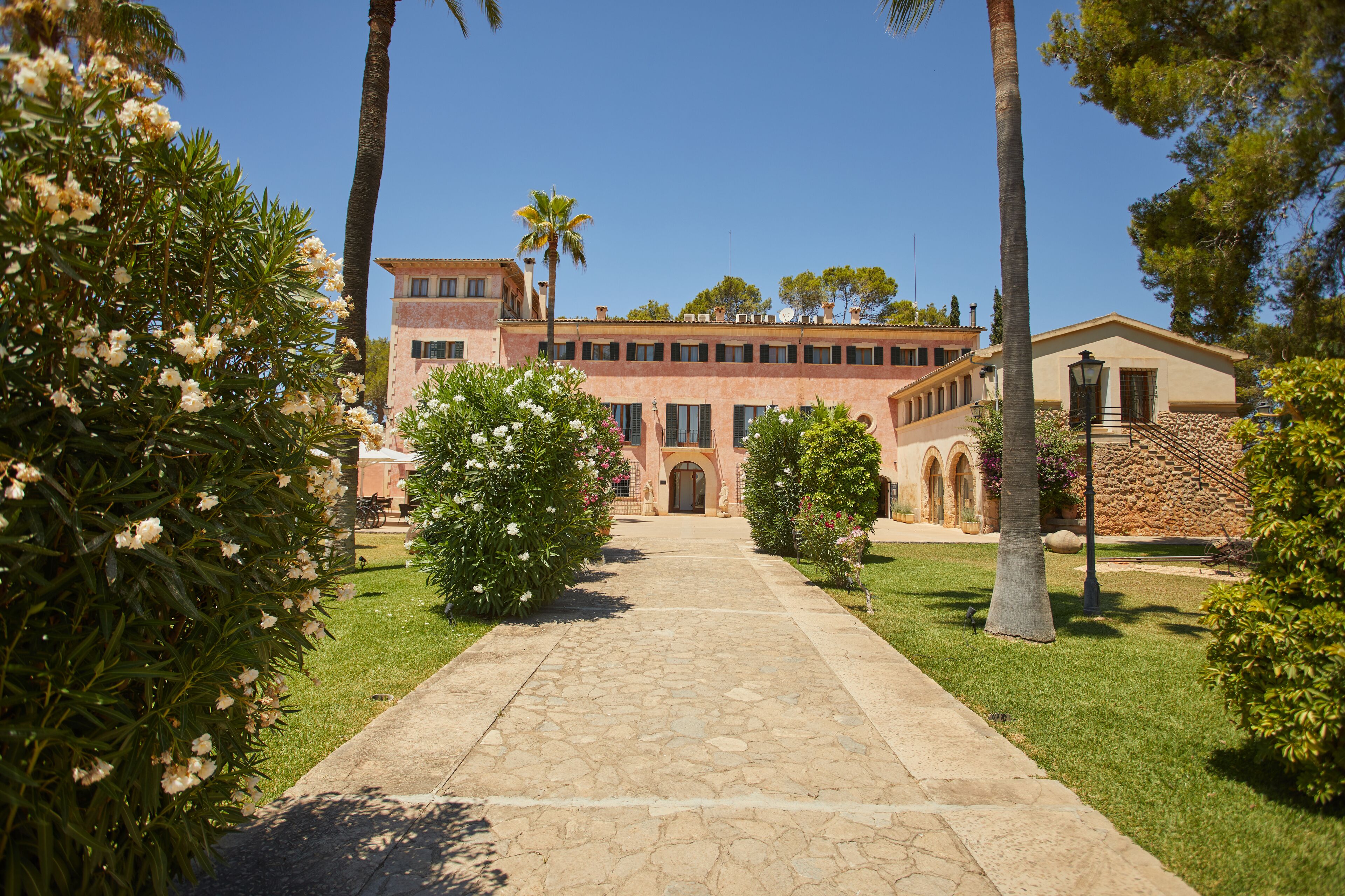 A pathway leading to a building with a stone facade, arched windows, and a central entrance.