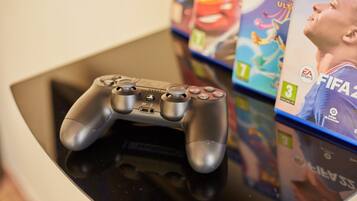 Un control de videojuego sobre una superficie reflectante, con fundas de videojuegos al fondo.