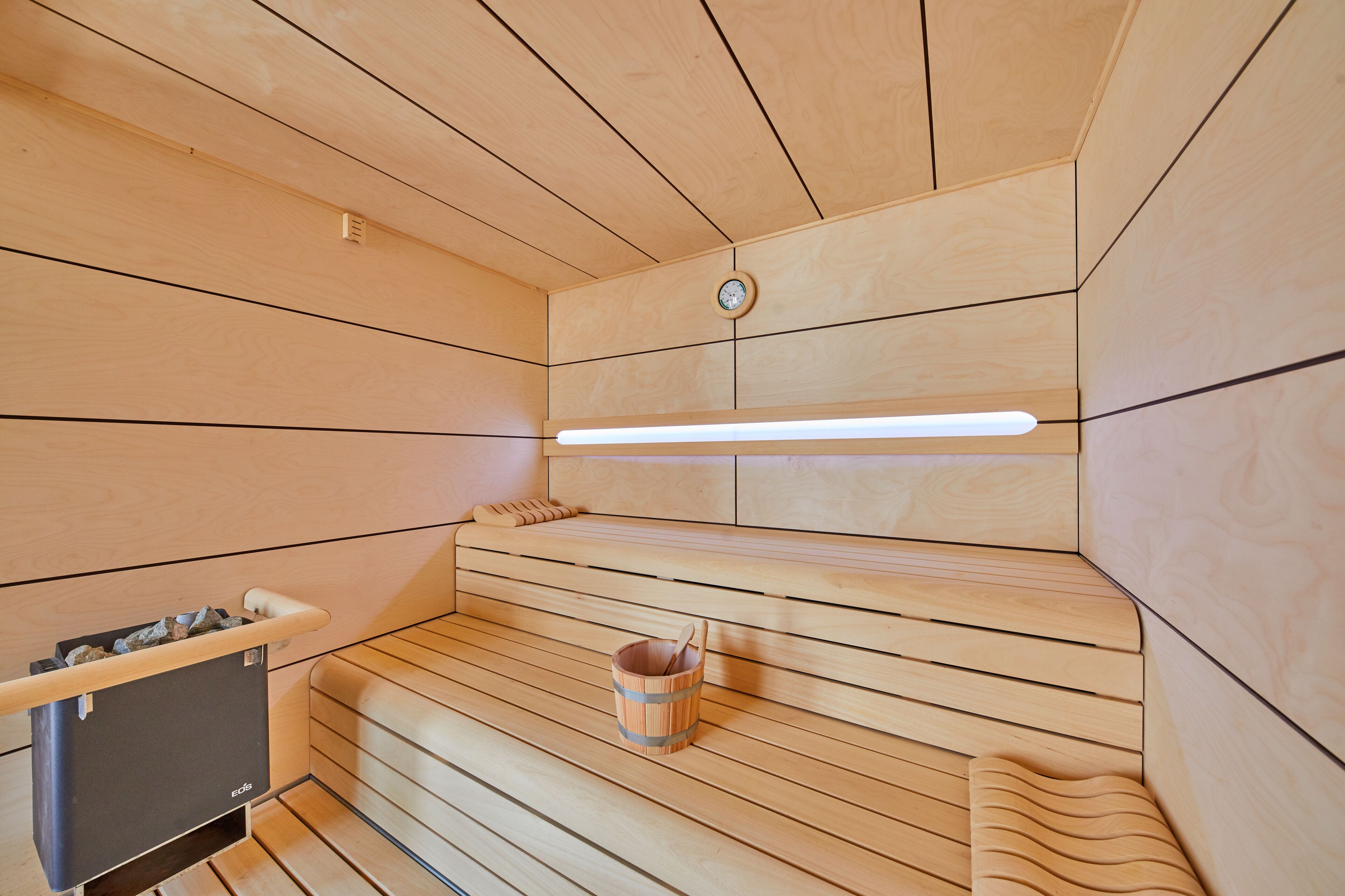 Eine Sauna mit Holzbänken, einem Holzeimer und einem Wandheizkörper.