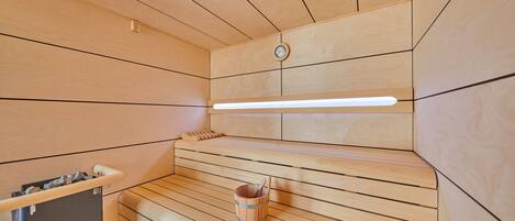 A sauna with wooden benches, a wooden bucket, and a wall-mounted heater.