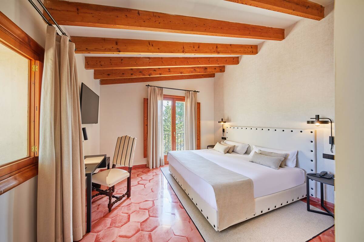 Une chambre avec un grand lit, des poutres en bois, un bureau et une chaise.