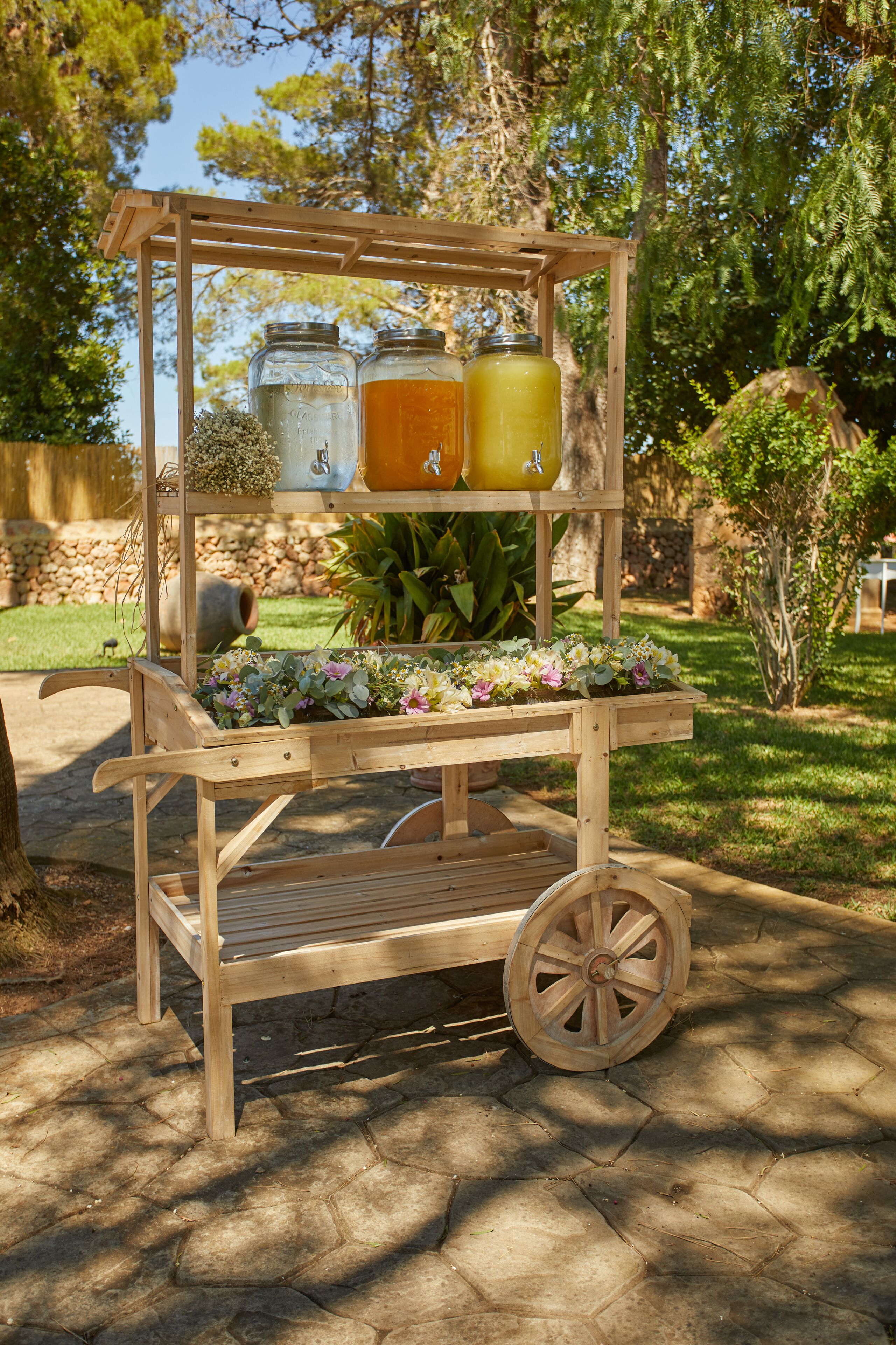 A wooden outdoor cart with jars and a flower arrangement.