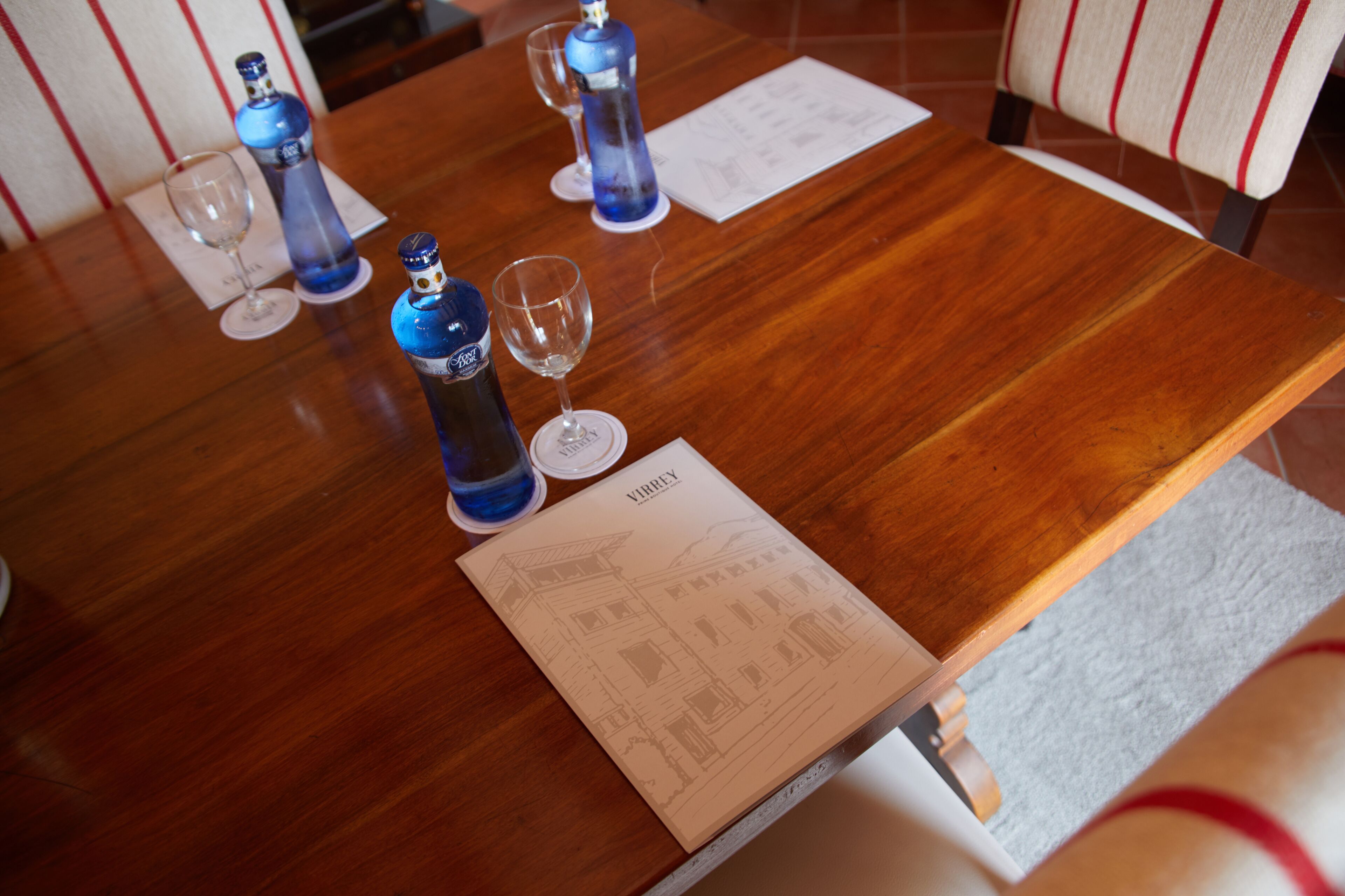 Une table en bois avec deux bouteilles bleues, deux verres à vin et un menu.