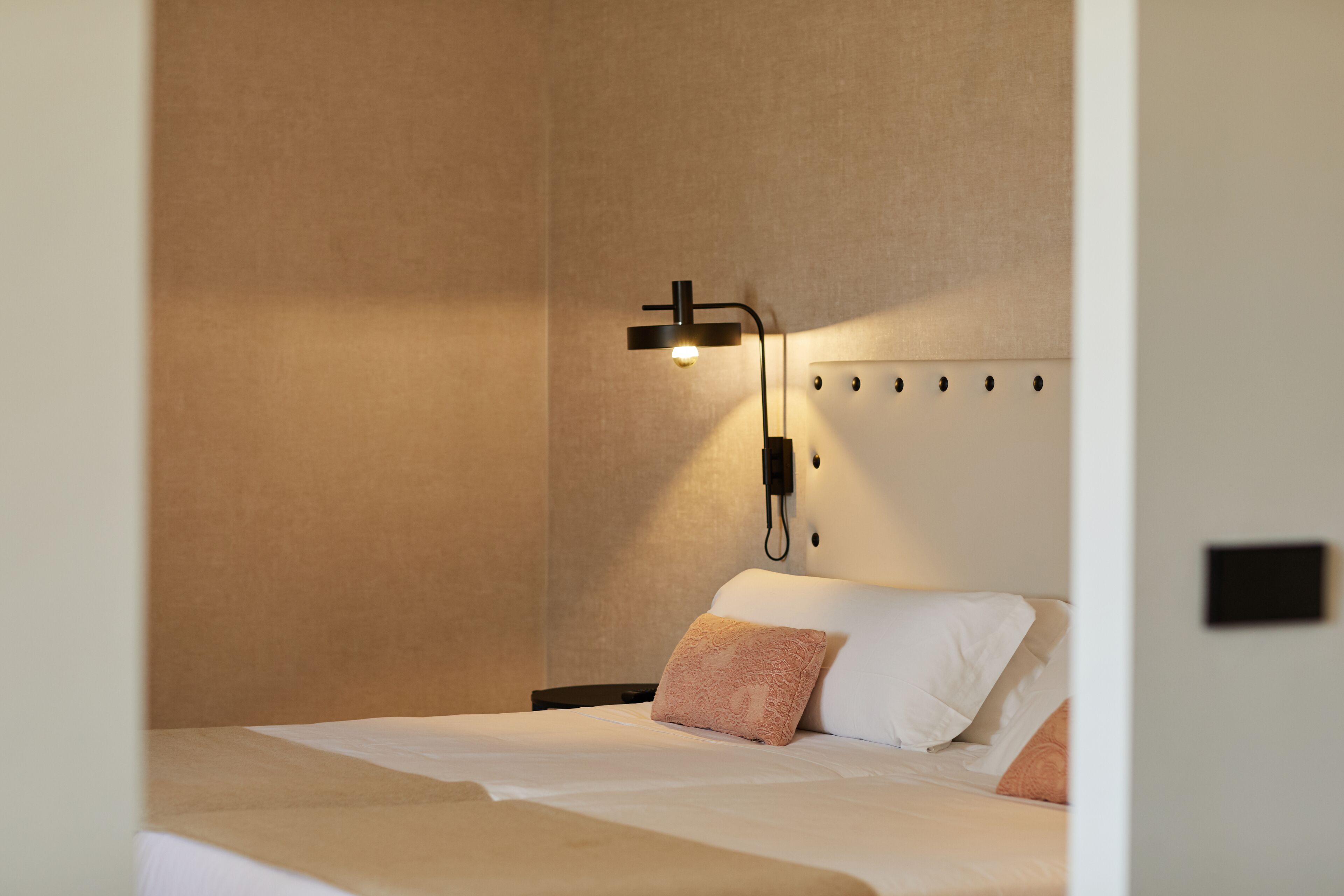A hotel room with a bed, a wall-mounted light fixture, and a power outlet.
