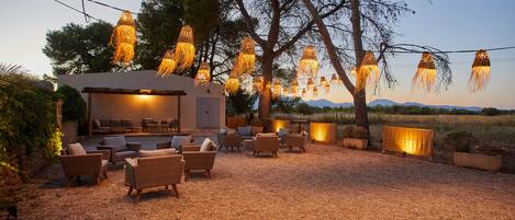 Un área de estar al aire libre con mobiliario de mimbre y luces colgantes.